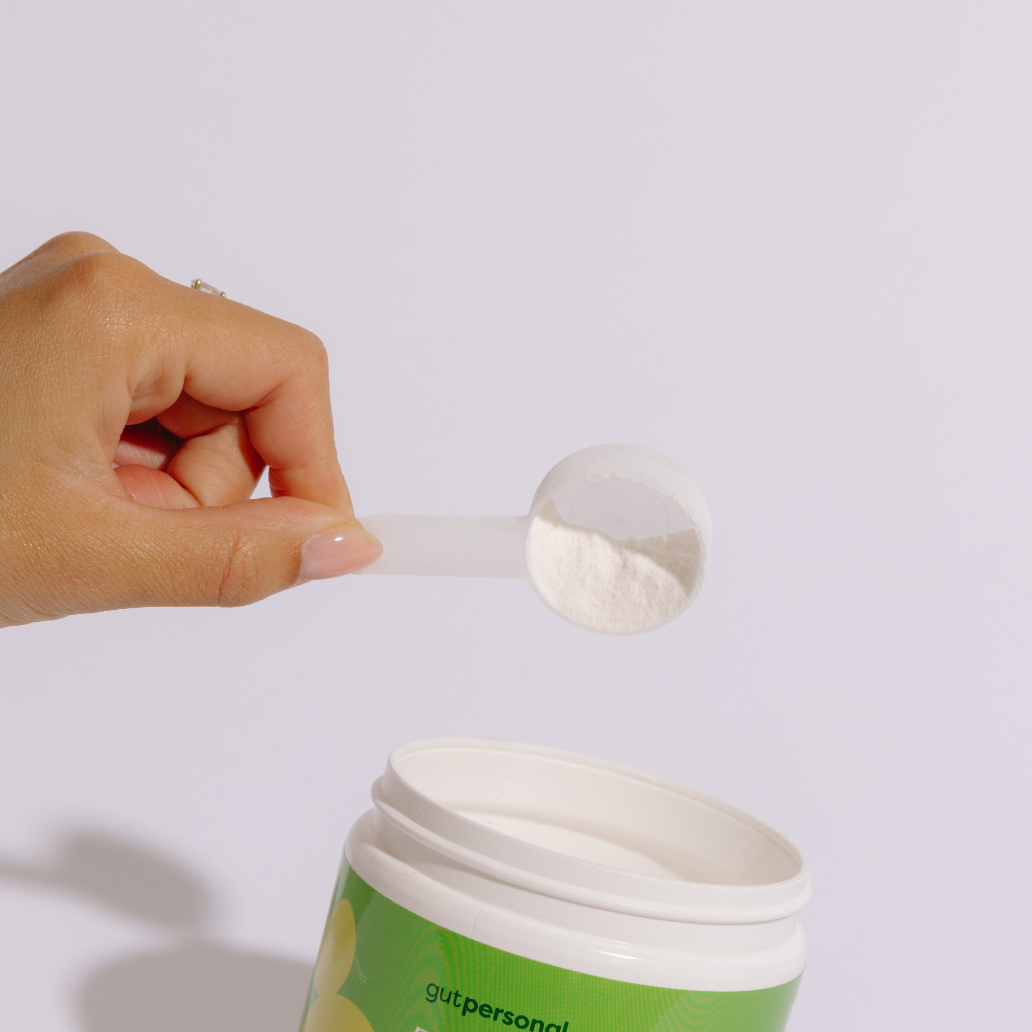 Hand scooping powder from a 'gutpersonal' container against a white background