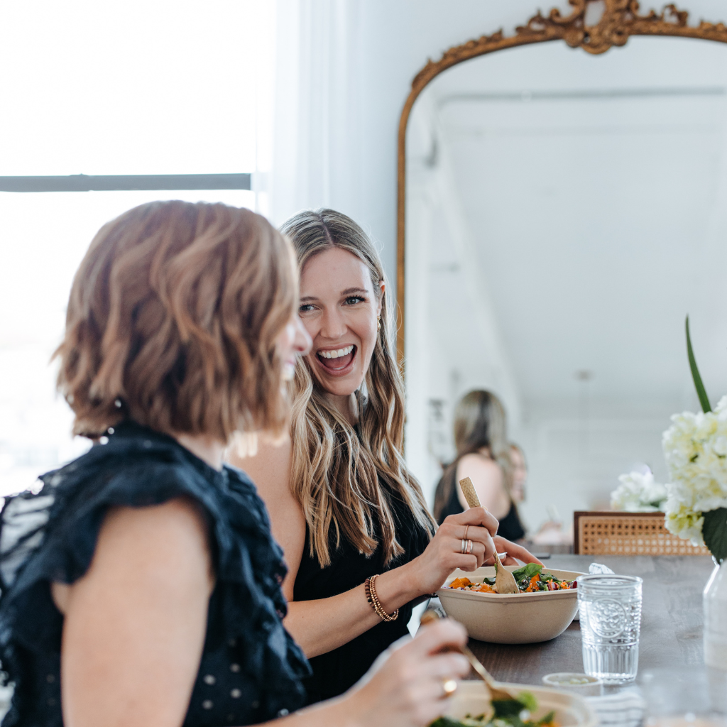 two women smiling while eating salads