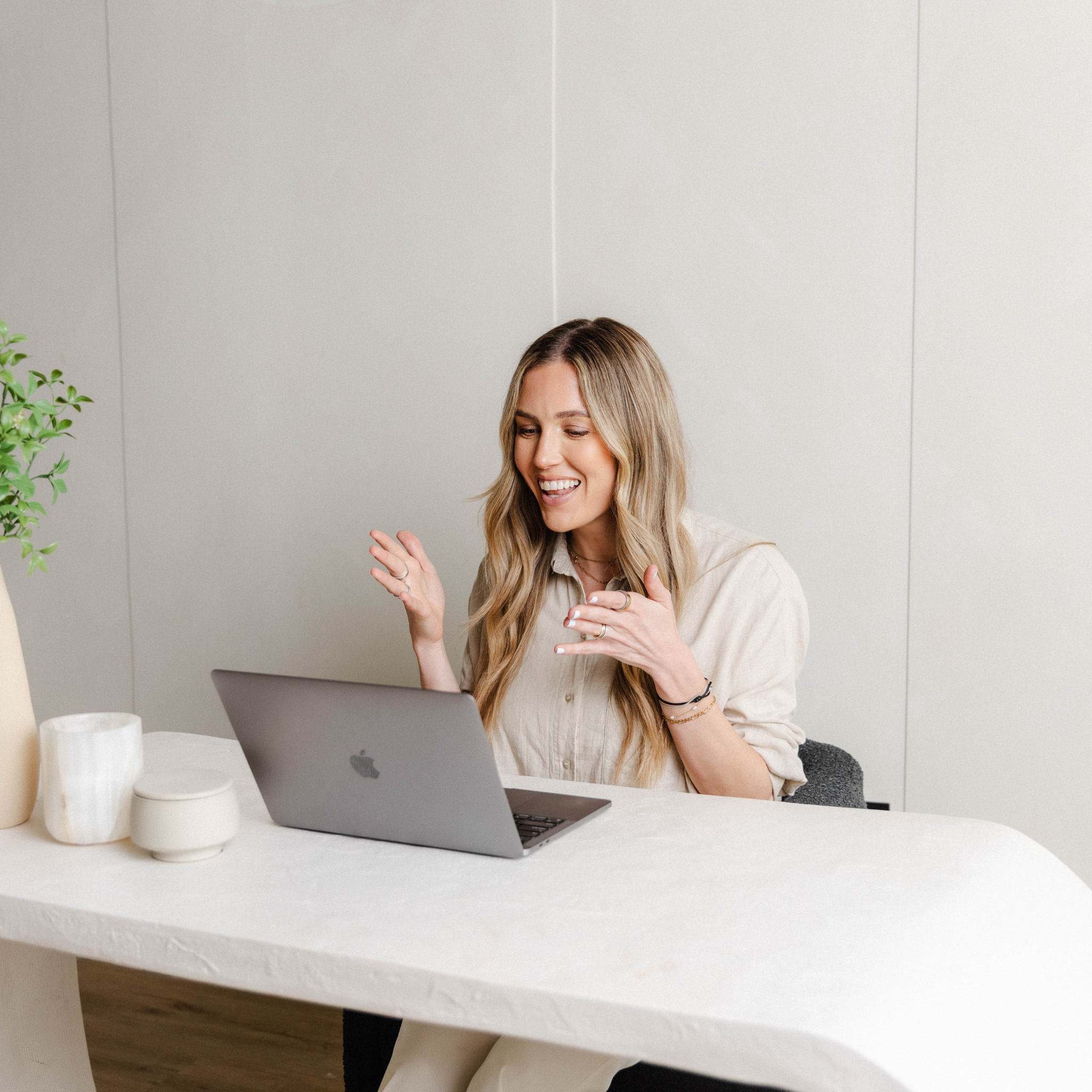 Woman sitting at a desk with a laptop, smiling and gesturing with her hands.
